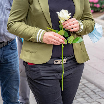 Frau mit einer weißen Rose in der Hand vor dem Körper